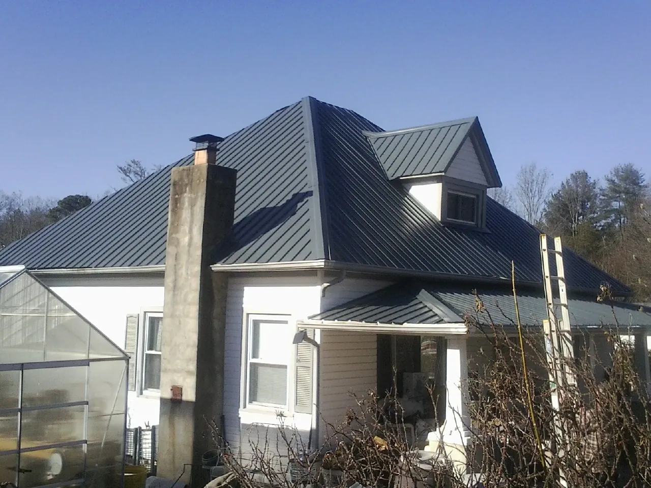 Dark blue standing seam metal roof on a white farmhouse with dormer — Slate & Tile Roof Repair by Roofing Brothers in Kirksville