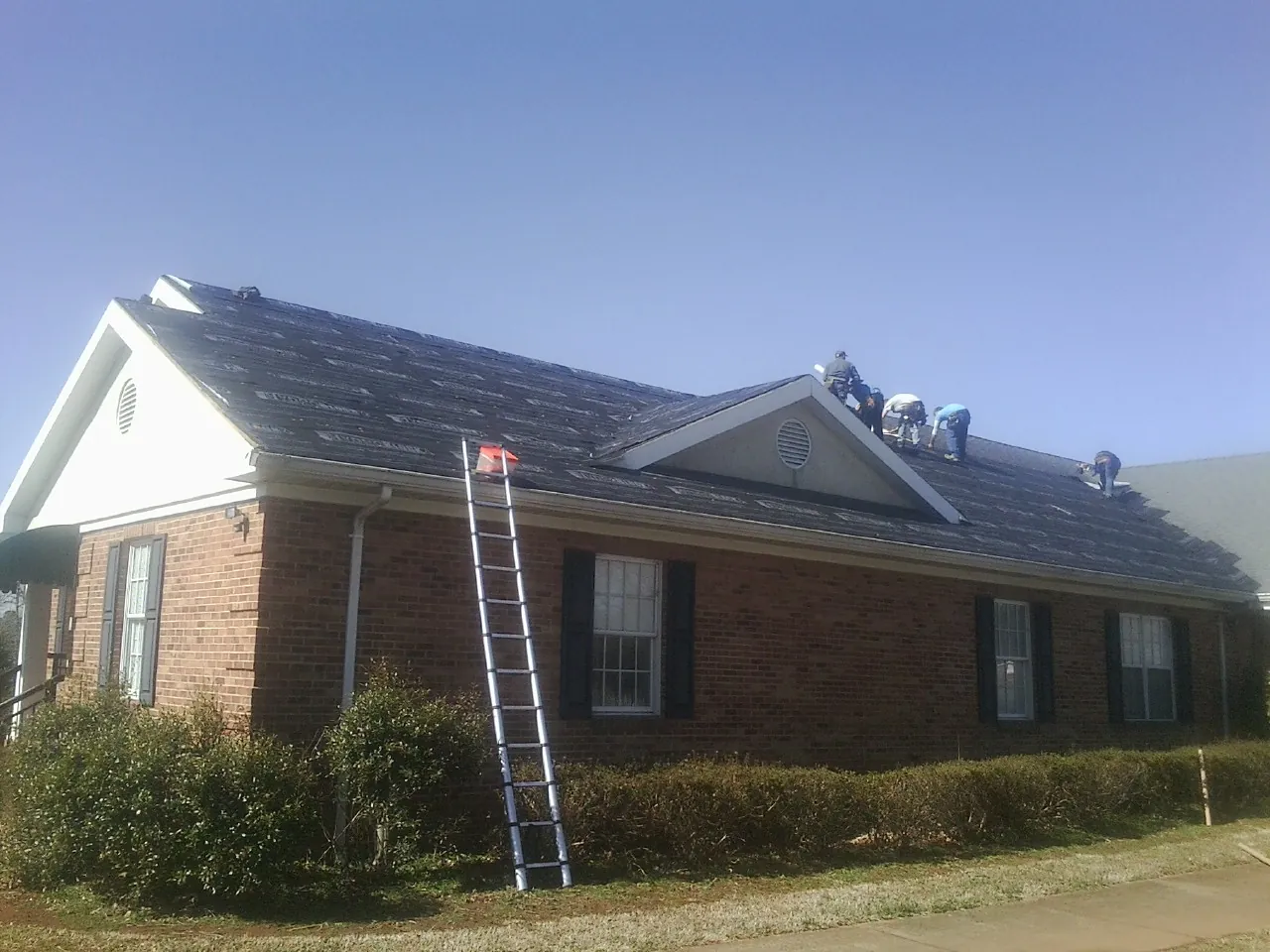 Crew tearing shingles off a brick ranch roof with a ladder set — Emergency Roof Repair work by our crew in Kirksville