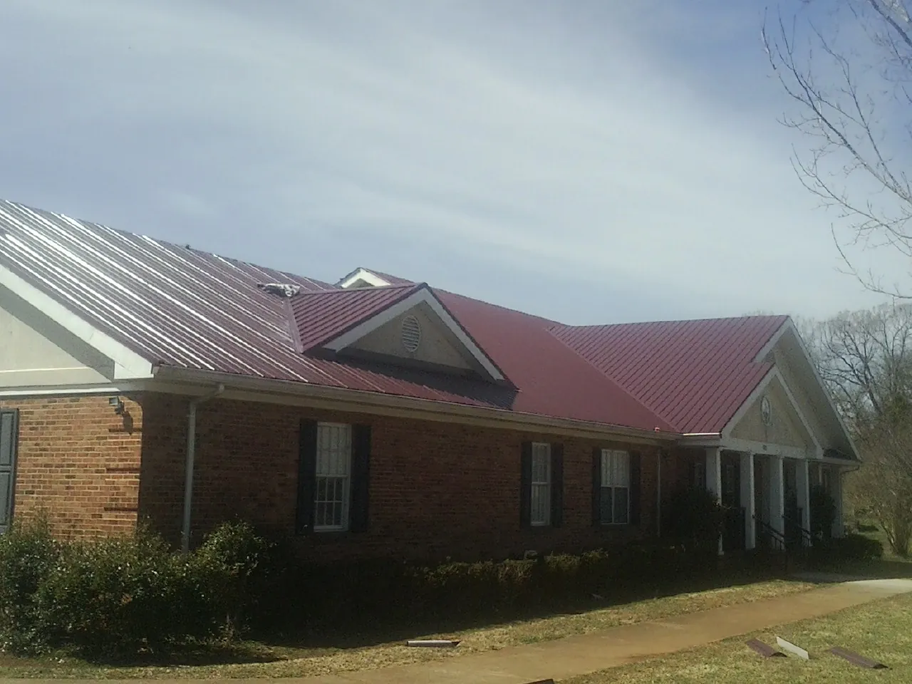 Red metal roof with gabled entries on a long brick building, from a Hail Damage Roof Repair job in Kirksville