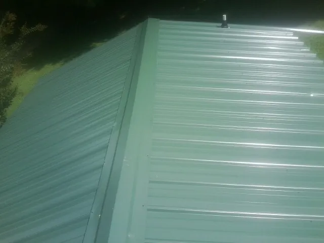 New green metal panels meeting at the ridge of a roof — Flat Roof Repair work by our crew in Kirksville
