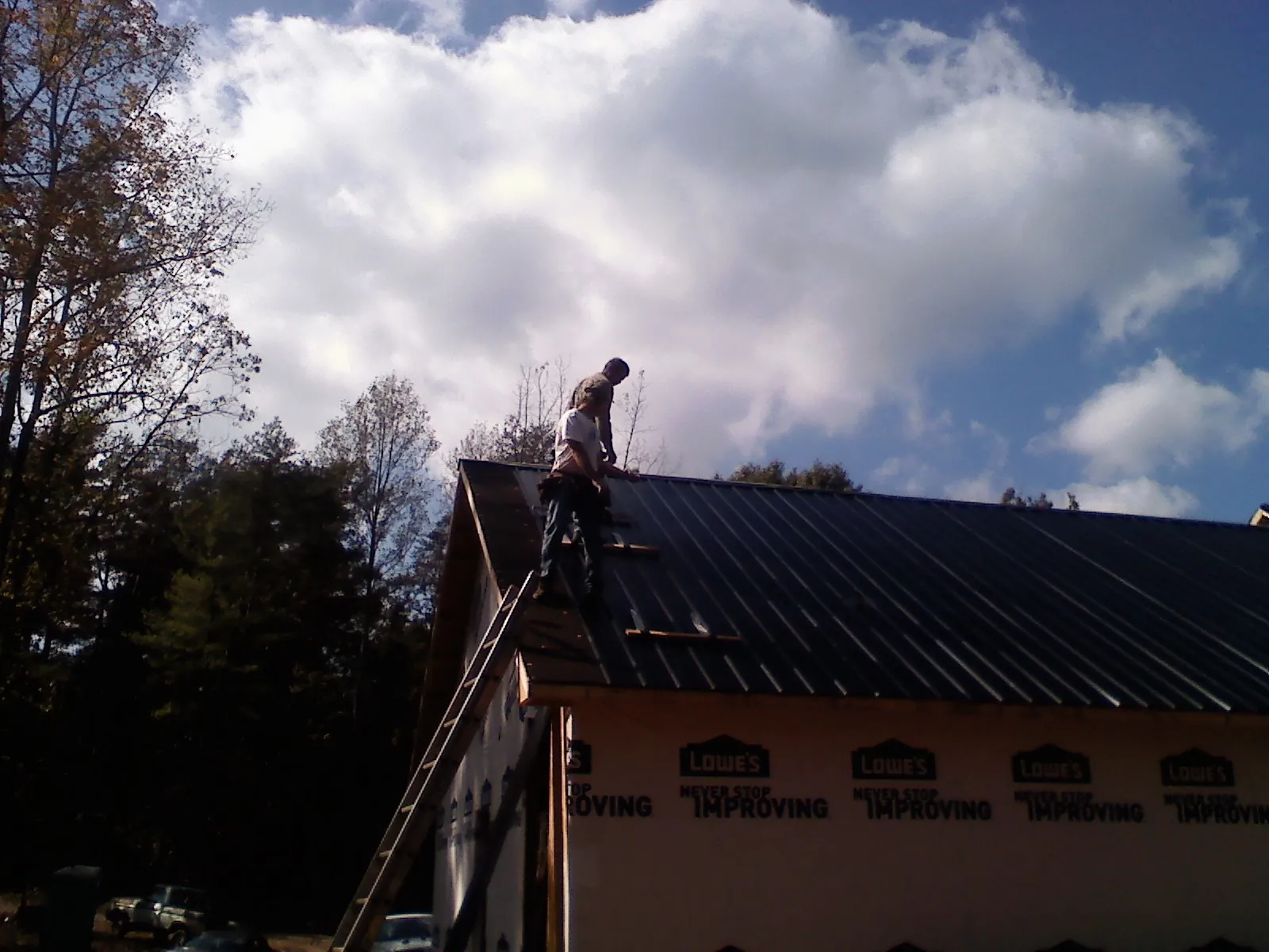Roofer fastening dark metal panels high against a cloudy sky, from a Roof Inspection job in Kirksville