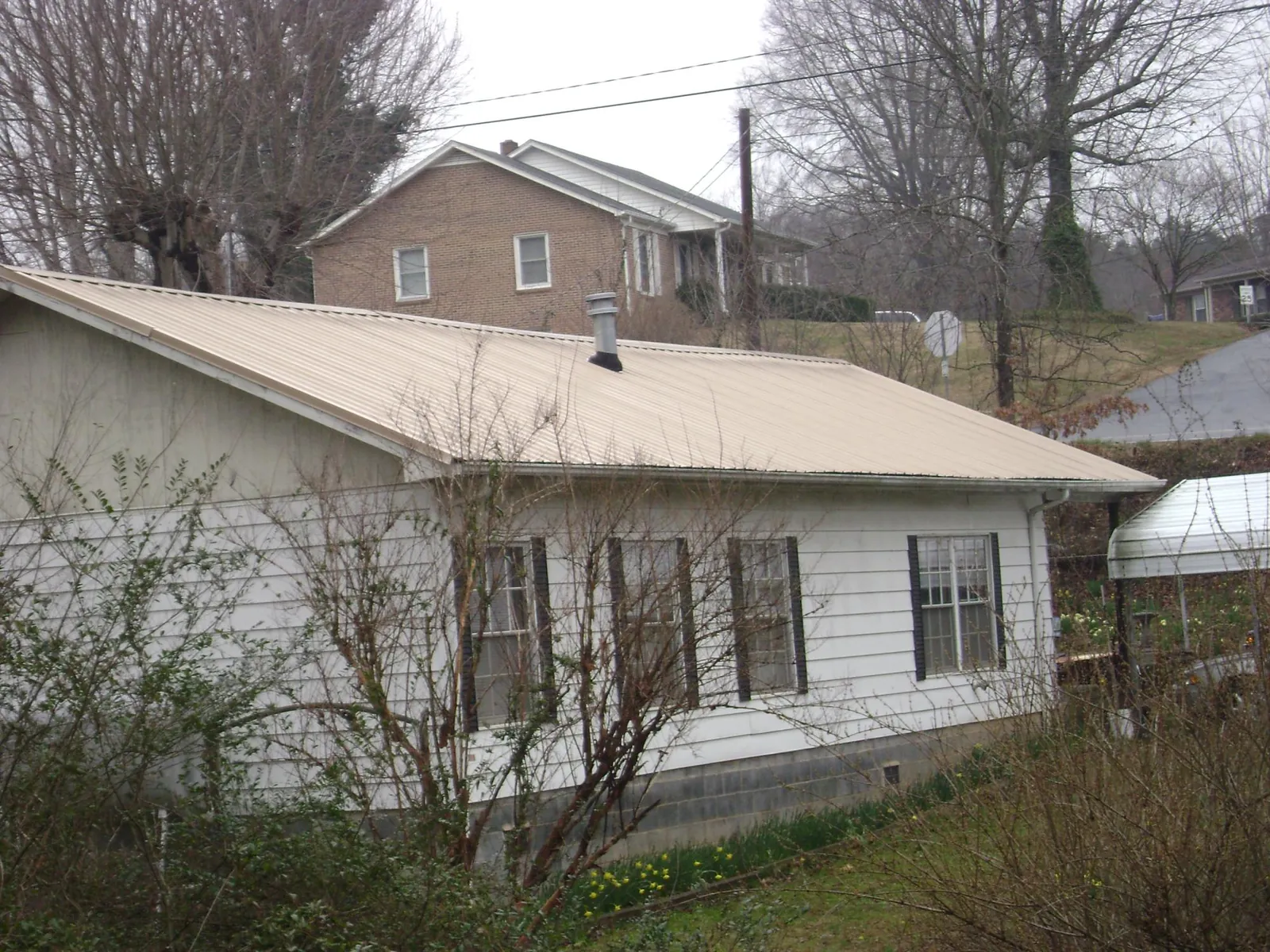 Tan metal roof on a white sided house set into a hillside — Commercial Roofing by Roofing Brothers in Kirksville