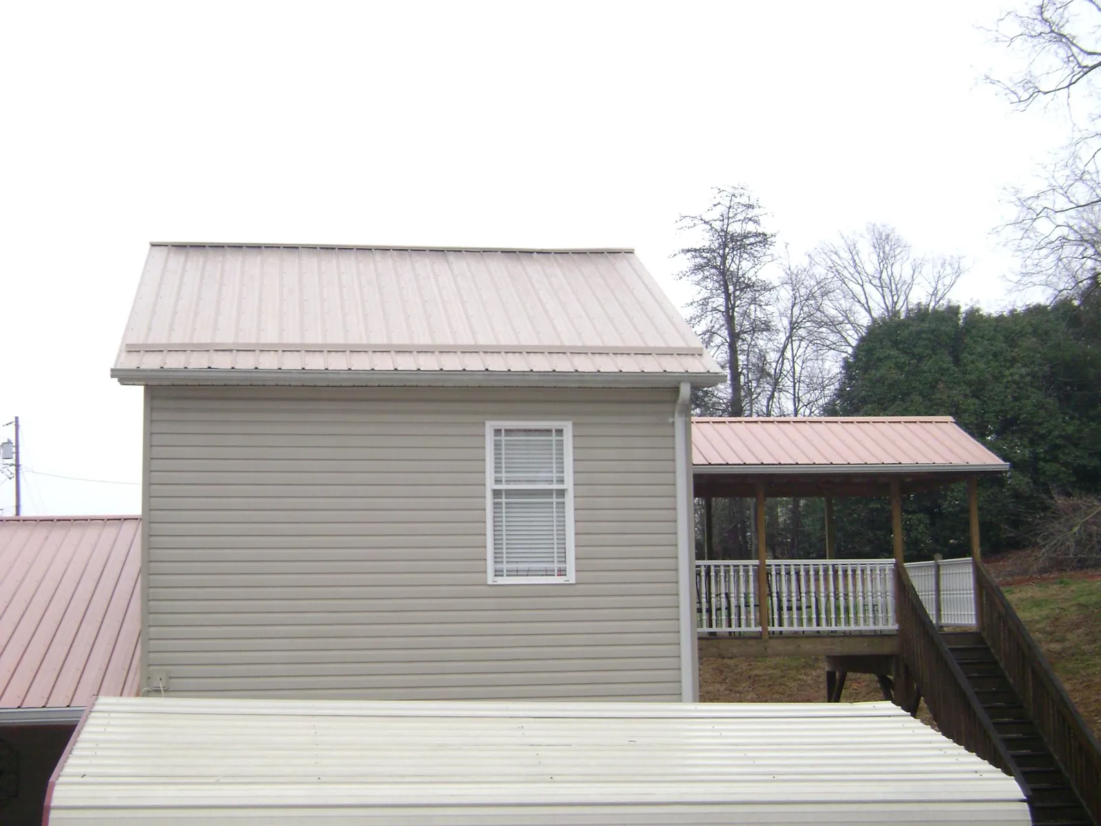 Tan metal roofs on a two story addition and attached porch, from a Roof Replacement job in Kirksville